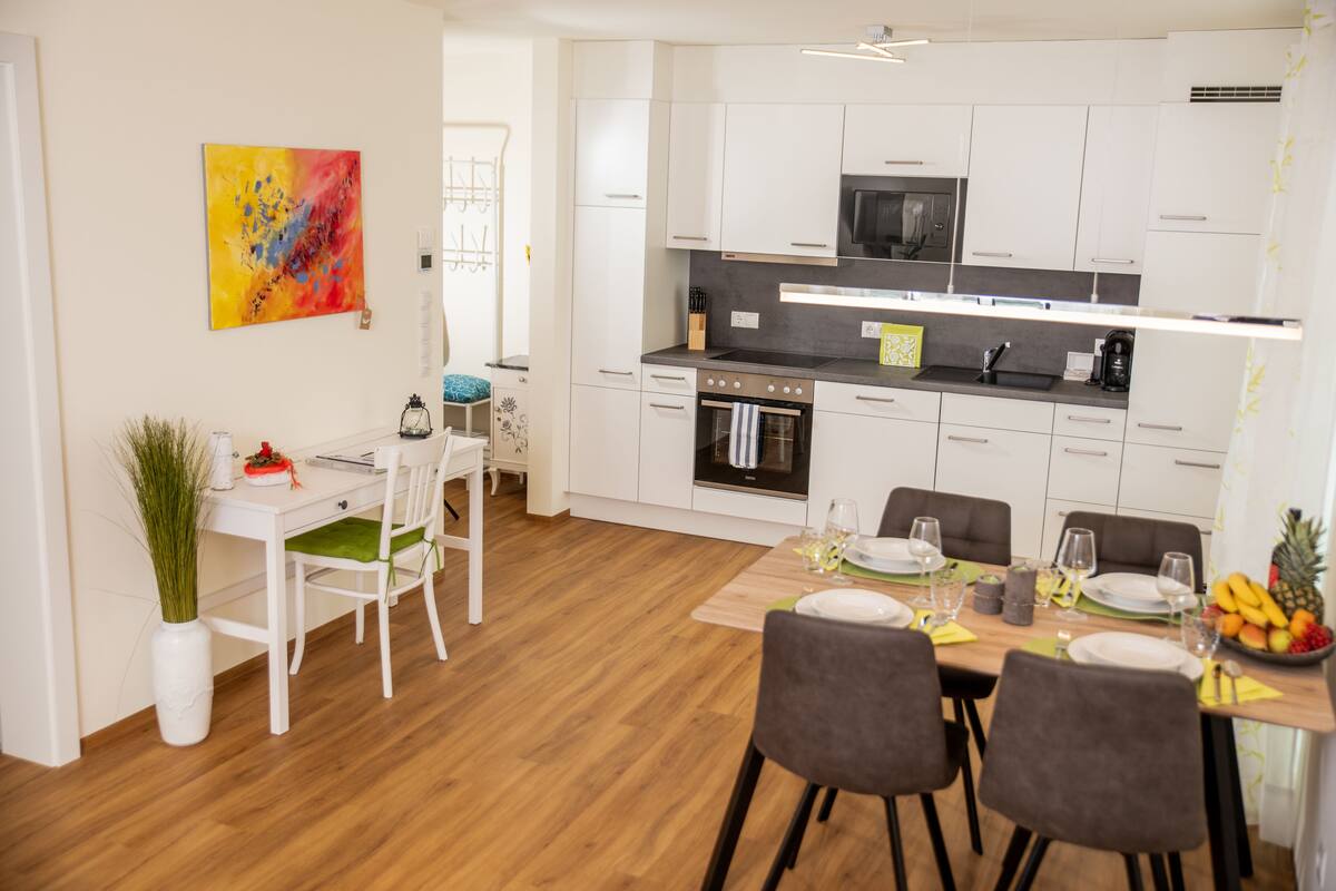 A modern kitchen with white cabinets, a black microwave, and a dining area with a wooden table set for four.