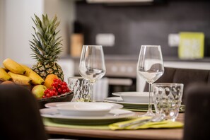 A dining table set with plates, glasses, and a fruit basket containing bananas, a pineapple, and red berries. - City Appartements Dornbirn (Dornbirn)