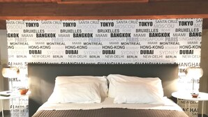 A hotel room with a bed, two bedside tables, and a wall with city names. - La Foresteria Garden Boutique B&B (Catania)