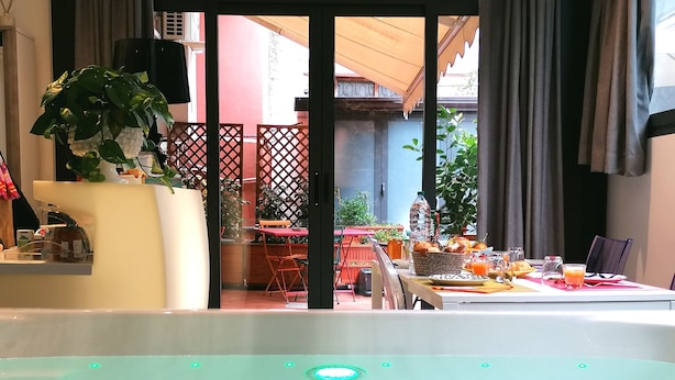 A room with a hot tub, a dining area with a table set for breakfast, and a view of the outside balcony. - La Foresteria Garden Boutique B&B (Catania)