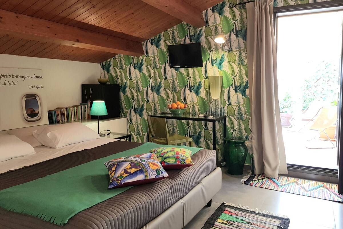 Une chambre à coucher avec un lit, une télévision, une bibliothèque, une table avec des fruits et une fenêtre avec des rideaux.