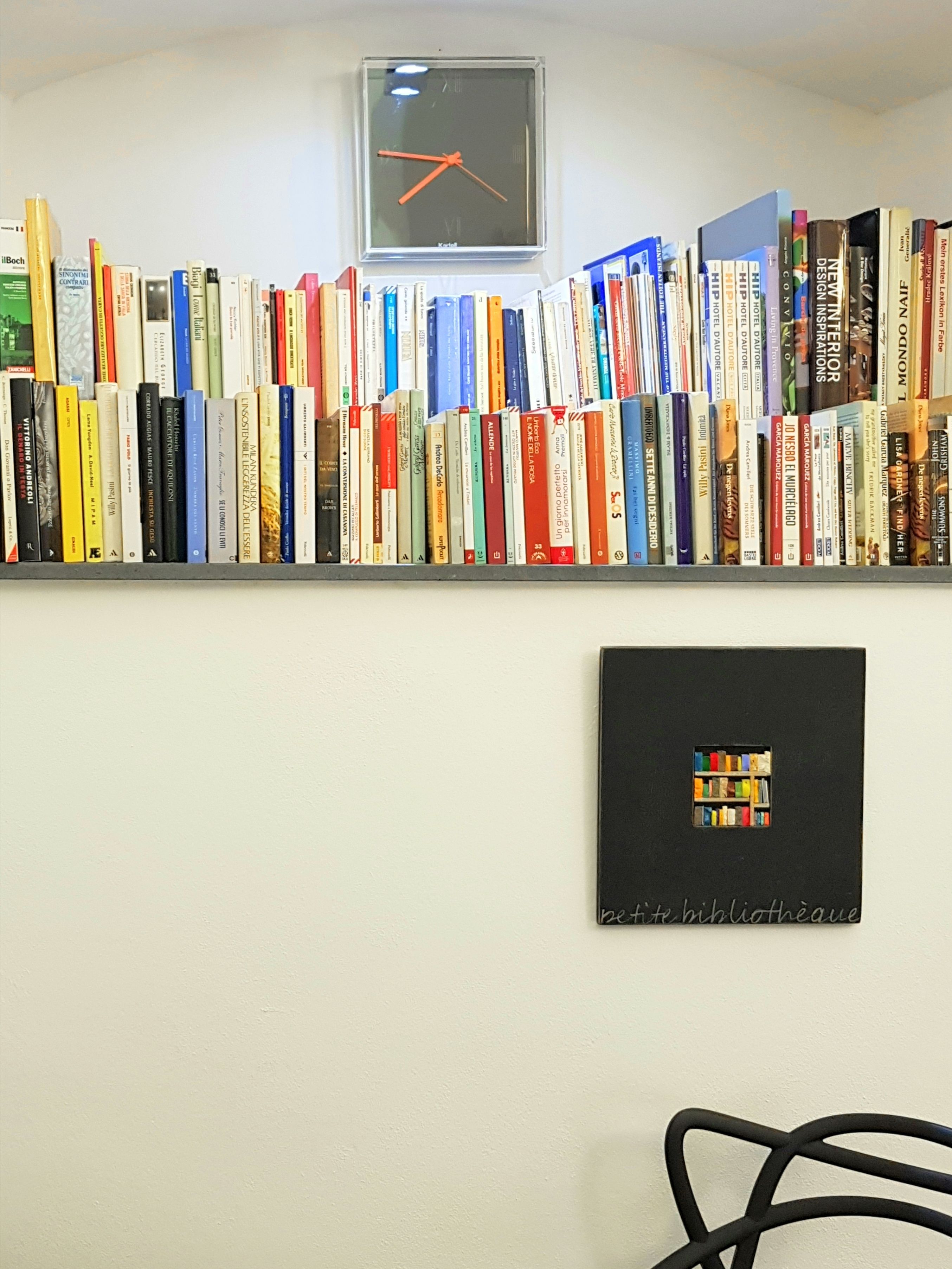 Un mur avec une bibliothèque remplie de livres et, en dessous, un tableau représentant des livres.