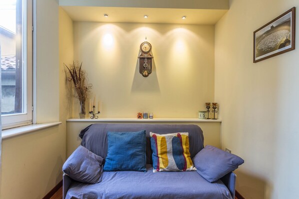 Um espaço acolhedor com área de estar estofada, um relógio fixado na parede e uma prateleira com objetos decorativos.