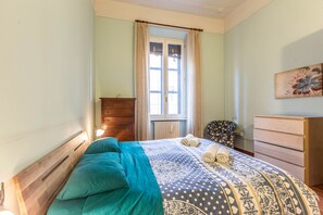 A bedroom with a bed, a wooden dresser, a chair, and a window with curtains.