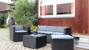 An outdoor patio with wicker furniture, a potted plant, and a wooden fence. - Auberge Leipzig (Leipzig)