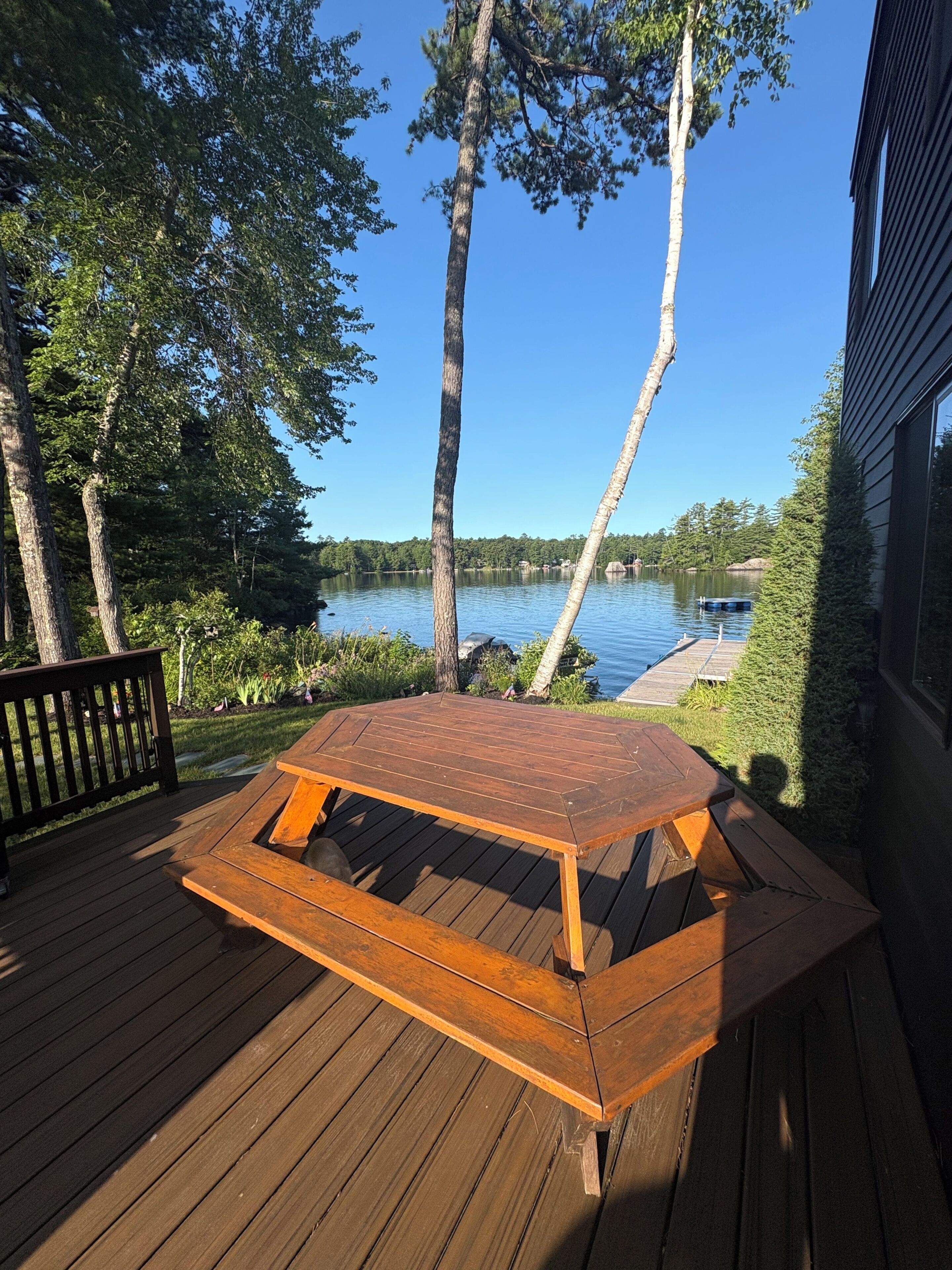 A wooden deck with a picnic table, overlooking a lake with trees and a dock.