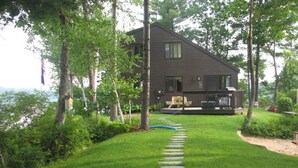 Une cabane dotée d’une terrasse, entourée d’arbres et accessible par un sentier bordé d’herbe.