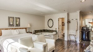 A spacious hotel room with a large bed, a sitting area with a chair, a bathtub, and a small kitchenette. - Leavenworth Village Inn (Leavenworth)
