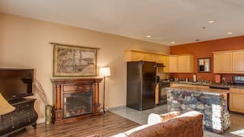 A spacious living room with a fireplace, a large TV, and a stone island in the kitchen area.