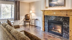 A living room with a fireplace, a sofa, a chair, and a lamp. - Leavenworth Village Inn (Leavenworth)