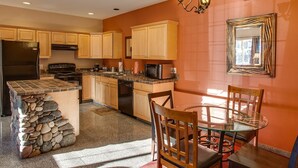 A kitchen with wooden cabinets, a stone island, and a dining area with chairs and a glass table. - Leavenworth Village Inn (Leavenworth)