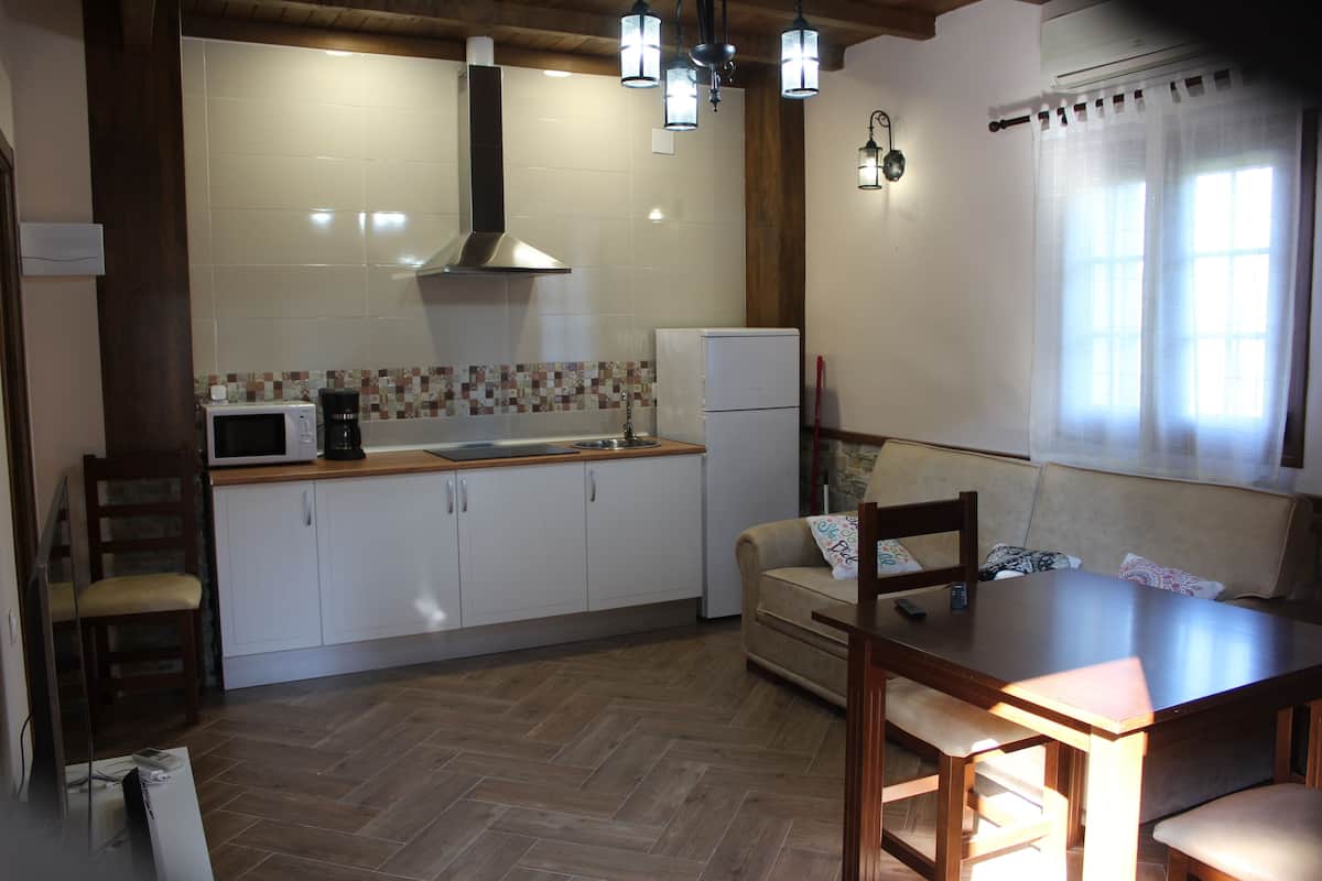 Une cuisine avec des meubles blancs, un four à micro-ondes, une machine à café et un réfrigérateur. On y trouve une table à manger et des chaises en bois.