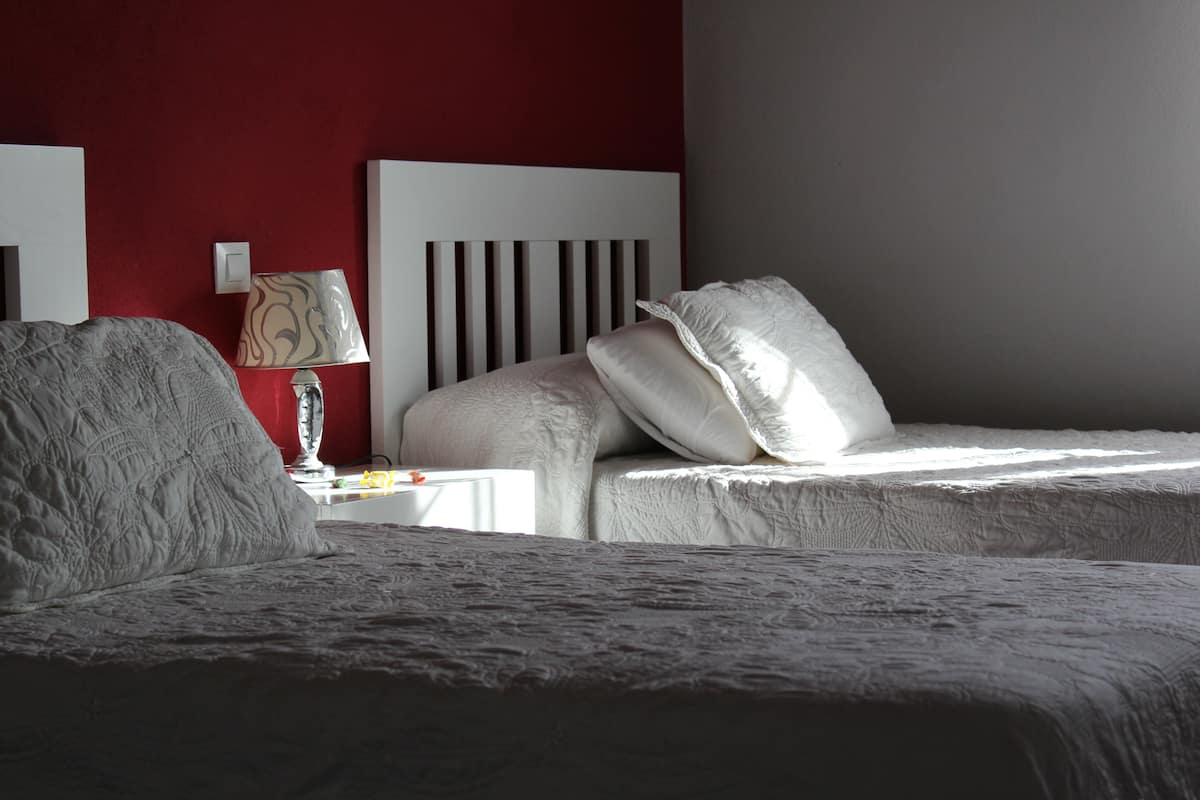 Une chambre avec deux lits, une table de chevet, une lampe et un mur d’accent de couleur rouge.