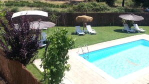Patio trasero con piscina, sillas de descanso y una sombrilla de paja.