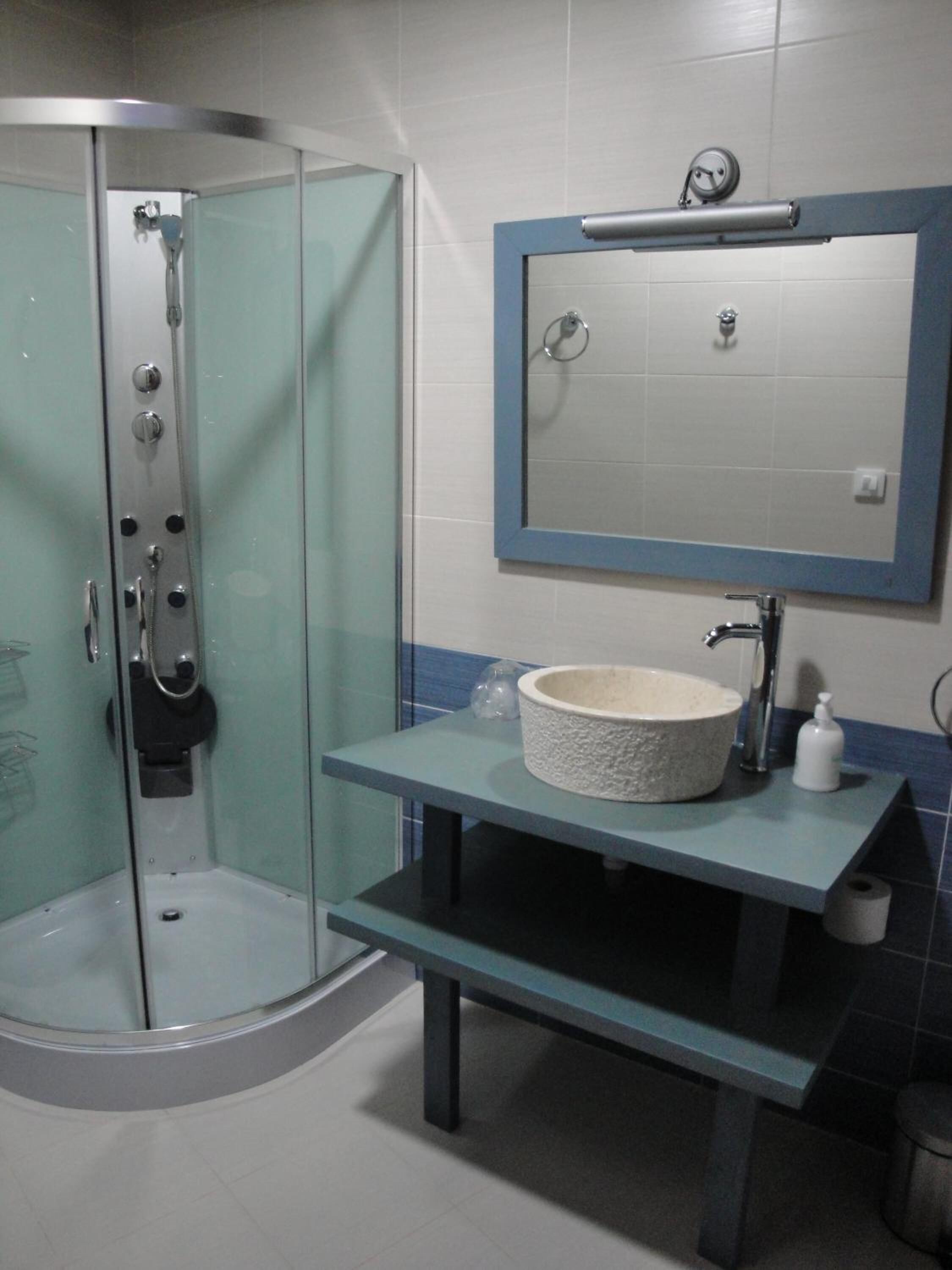 Un baño con ducha envuelta en vidrio, un lavabo de piedra y un espejo sobre él.