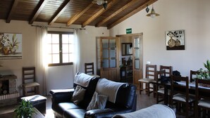 Una sala acogedora con un sofá de cuero, una mesa de comedor de madera y sillas. Se ve una chimenea en una esquina, y hay una puerta con la leyenda "SALIDA".