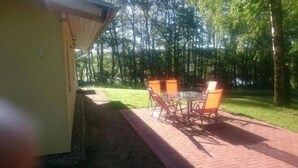 A patio with a table and chairs, surrounded by a grassy area and trees. - Ferienhäuser Seewiesen (Alt Schwerin)