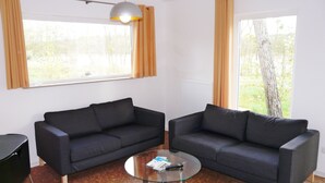 A modern living room with two black sofas, a glass coffee table, and a pendant light. - Ferienhäuser Seewiesen (Alt Schwerin)