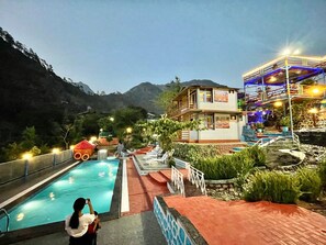 Uma área de piscina com vista para montanhas, um edifício com varanda e uma escadaria que leva a um terraço com guarda-corpo.