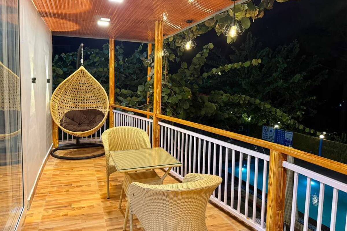 Ein Balkon mit Korbmöbeln, einem Hängesessel und Blick ins Grüne bei Nacht.