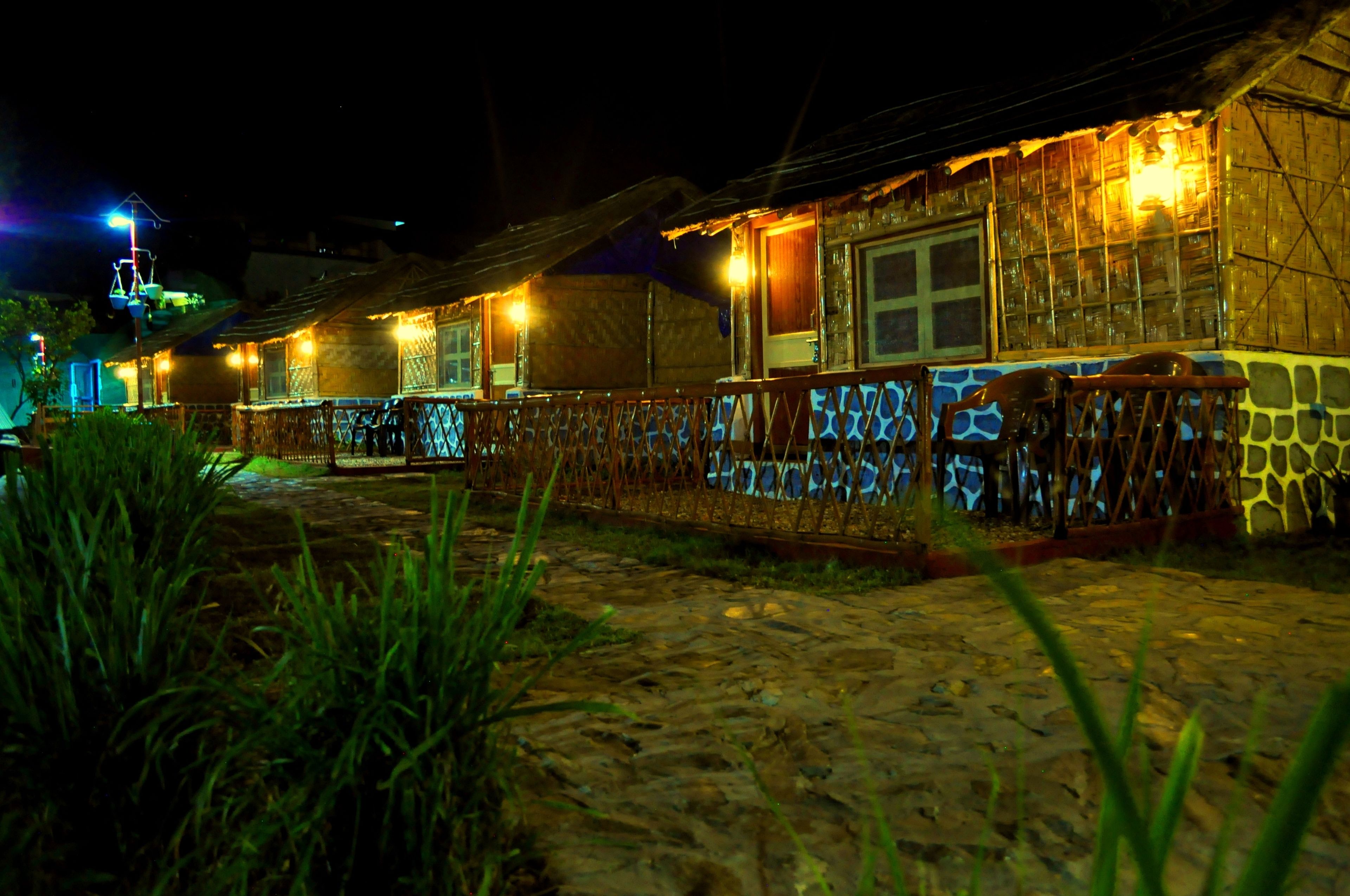A row of rustic, illuminated cabins with a stone pathway leading to them.