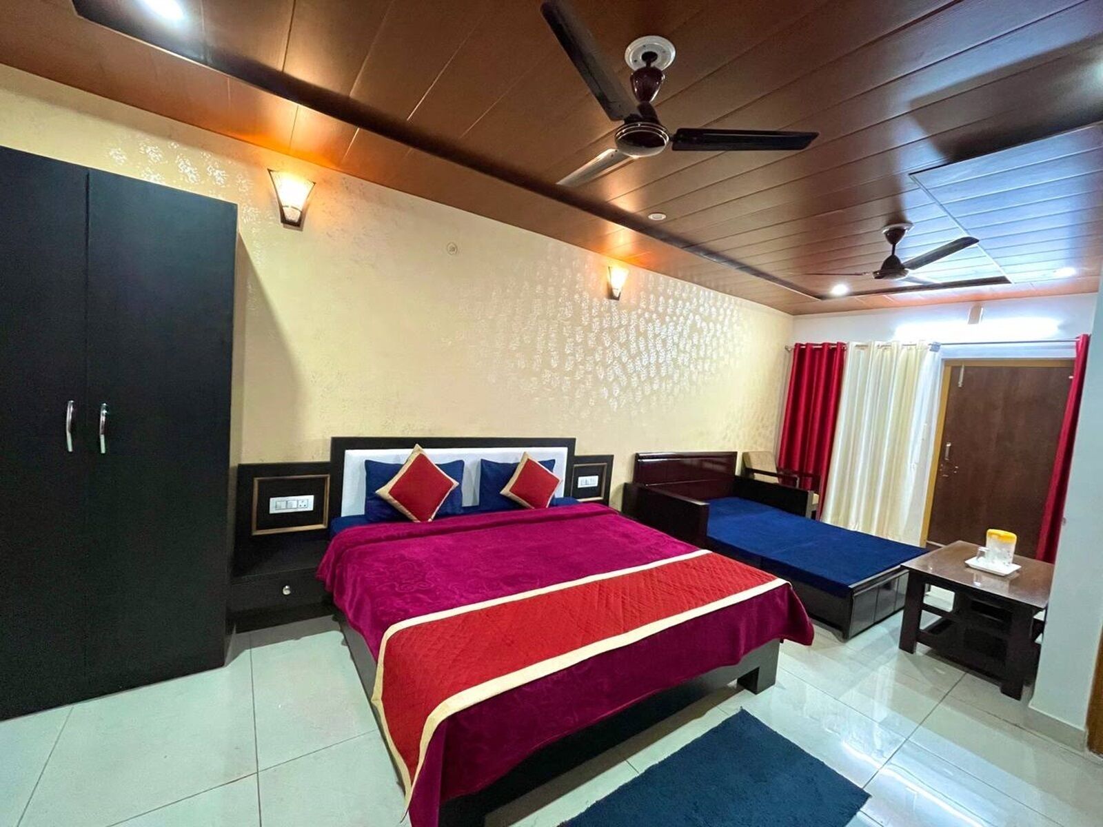 A hotel room with a large bed, a wardrobe, a desk, and a ceiling fan.