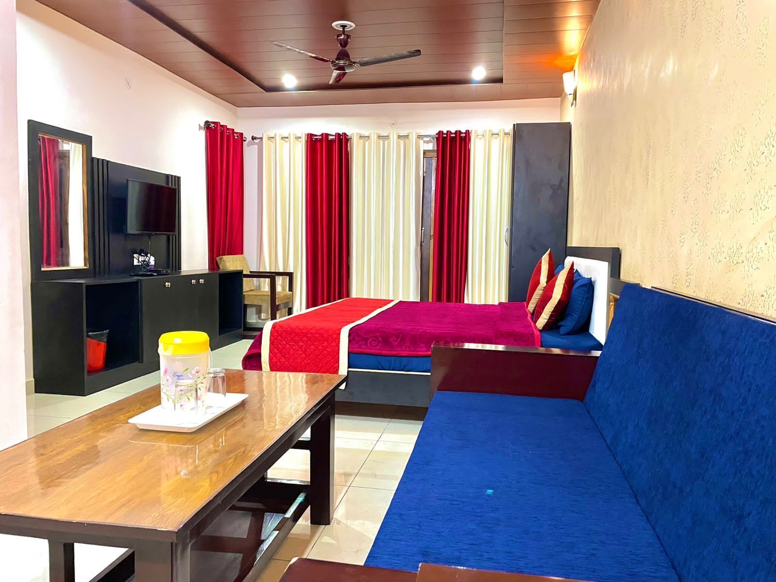 A hotel room with a bed, a sofa, a TV, a desk, and a ceiling fan.