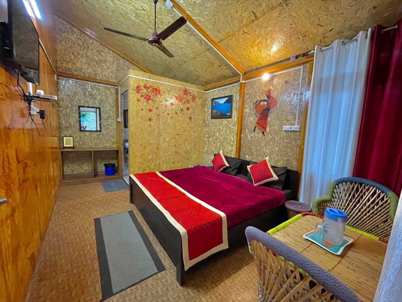 Una habitación acogedora con cama, una mesita, una silla, ventilador de techo y televisor.