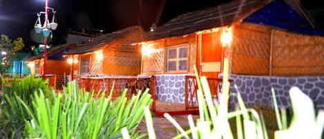Une rangée de cabanes rustiques aux murs de pierre et aux toits en bois, illuminées par une lumière chaleureuse.