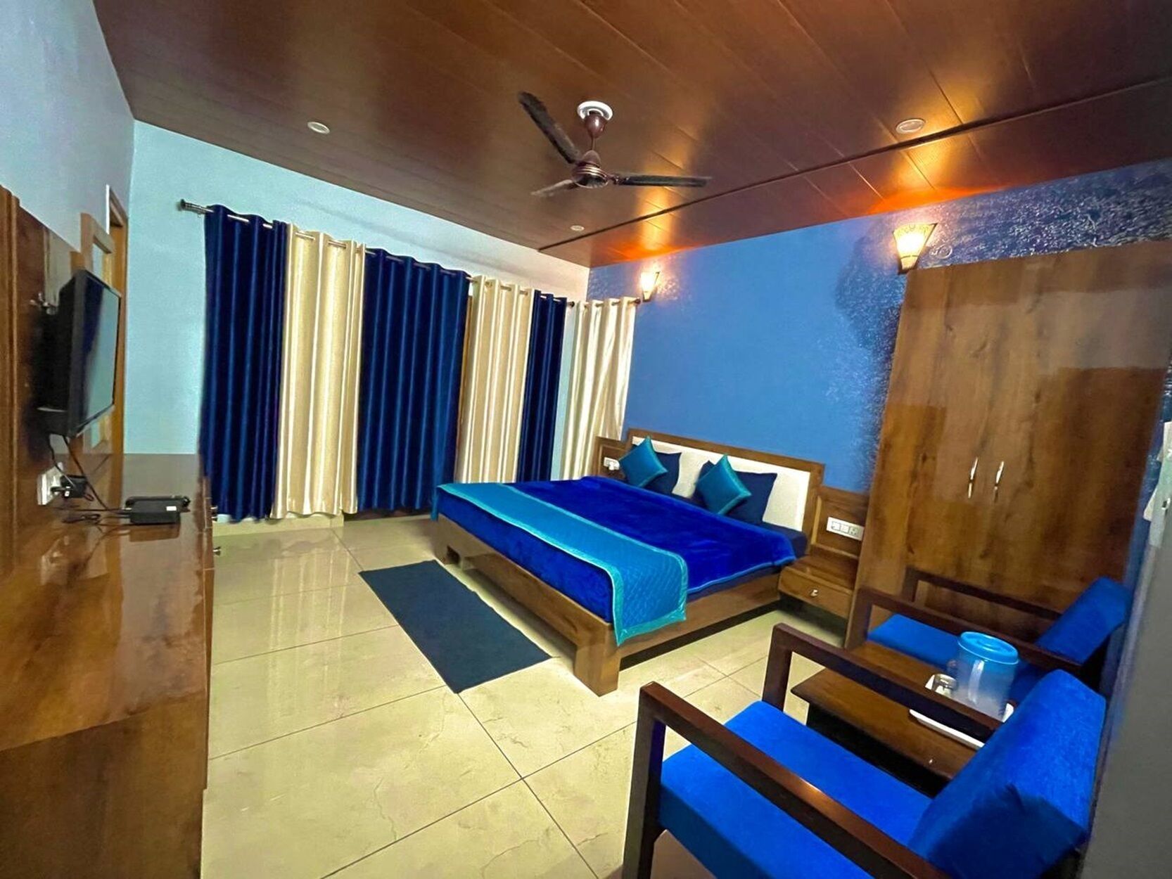 A hotel room with a bed, a desk, a chair, a wardrobe, and a ceiling fan.