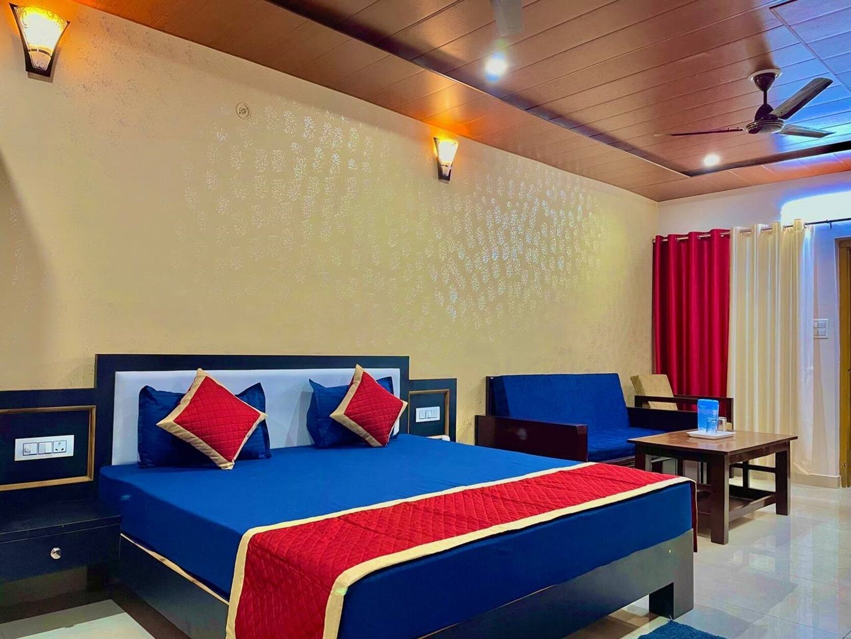 A hotel room with a large bed, two bedside tables, a desk, and a ceiling fan.