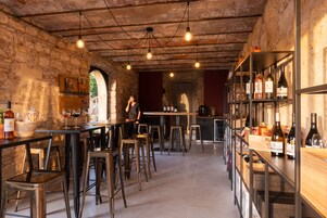 Un rústico espacio de bar con paredes de ladrillo visto, estantes de madera con botellas de vino y taburetes de metal.