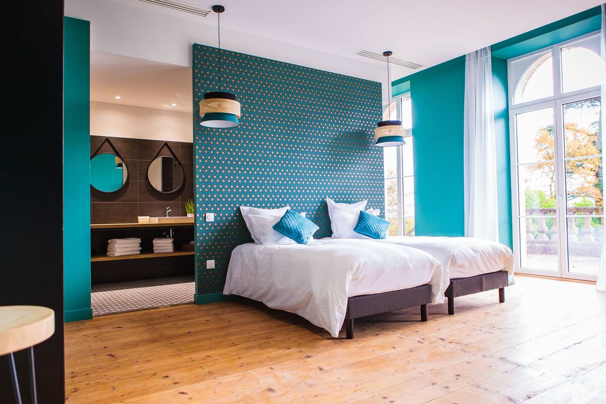 Une chambre moderne avec deux lits, une grande fenêtre et un mur d’accent de couleur turquoise.