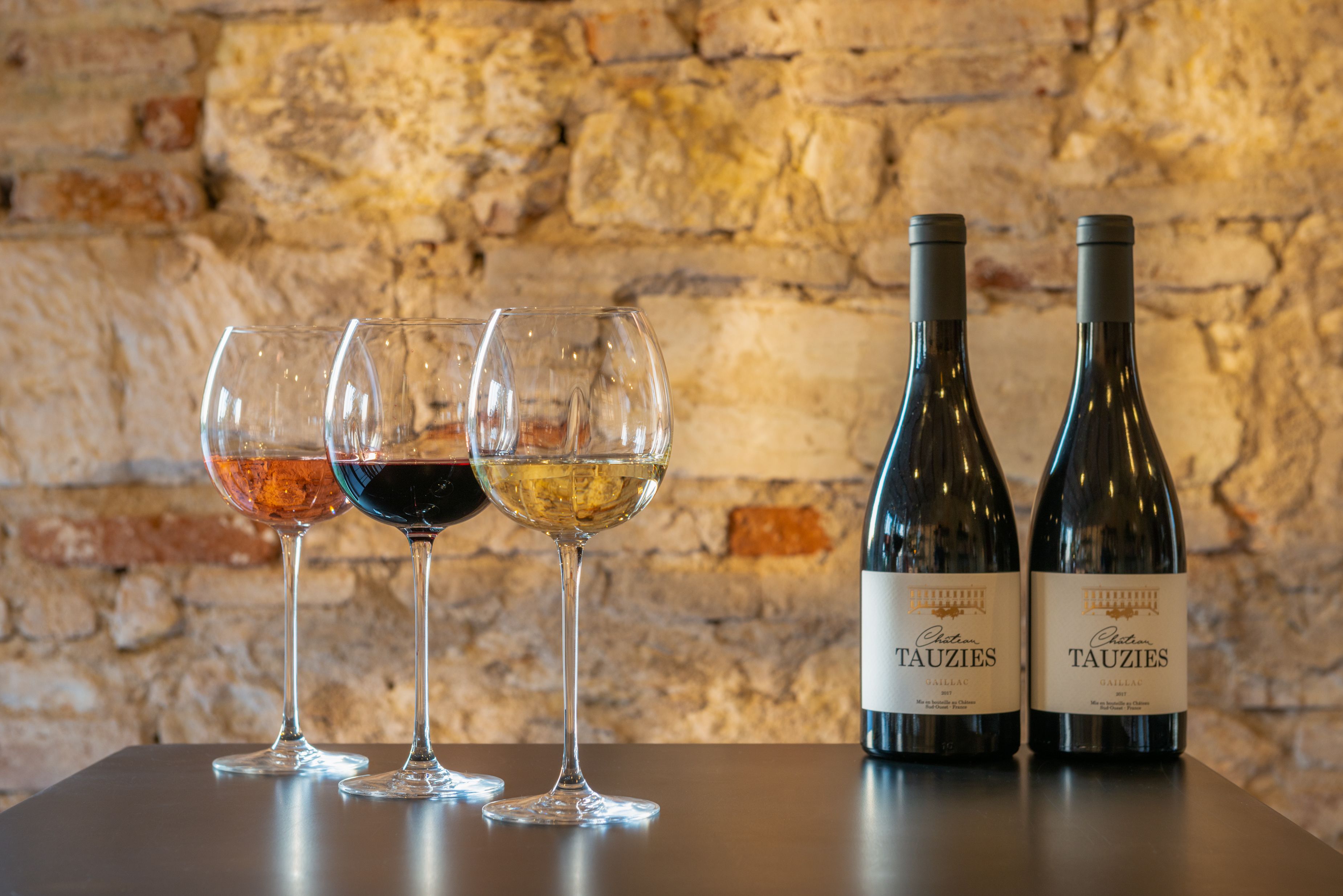 Two bottles of wine and three glasses on a table against a stone wall.