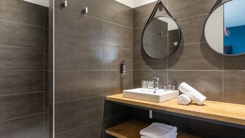 A modern bathroom with dark tiles, a wooden vanity, a sink, a mirror, and a shower area.