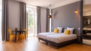 Een moderne hotelkamer met een groot bed, een tafeltje, gele stoelen en uitzicht op de omgeving.