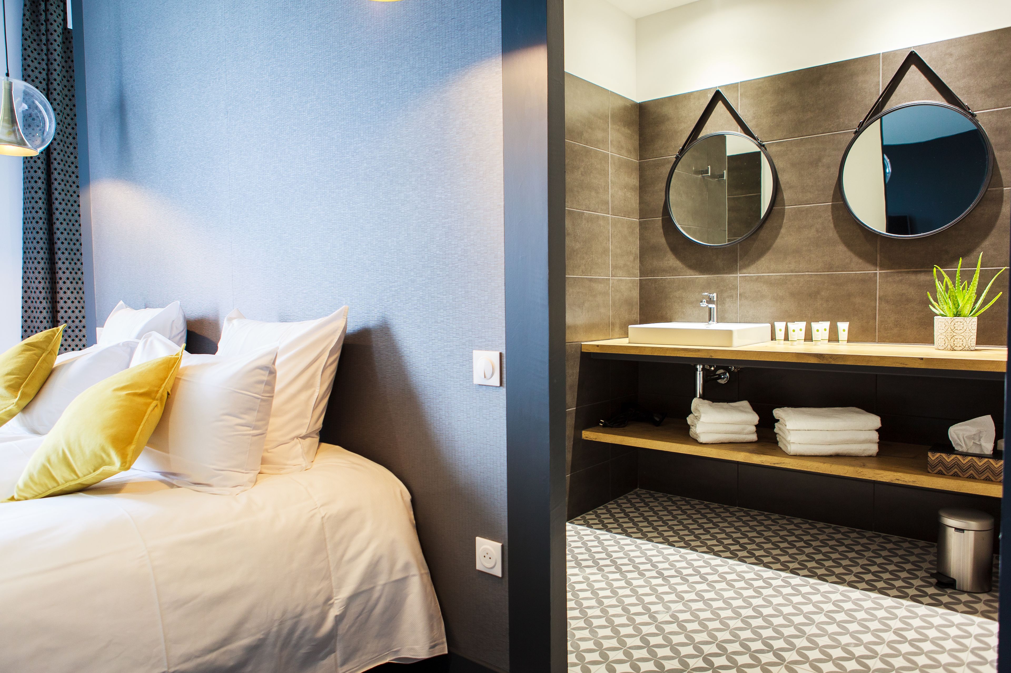 Een hotelkamer met een bed, een badkamer met een spiegel, een wastafel en een potplant.