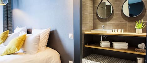 Una habitación de hotel con cama, baño con espejo, lavabo y planta en maceta.