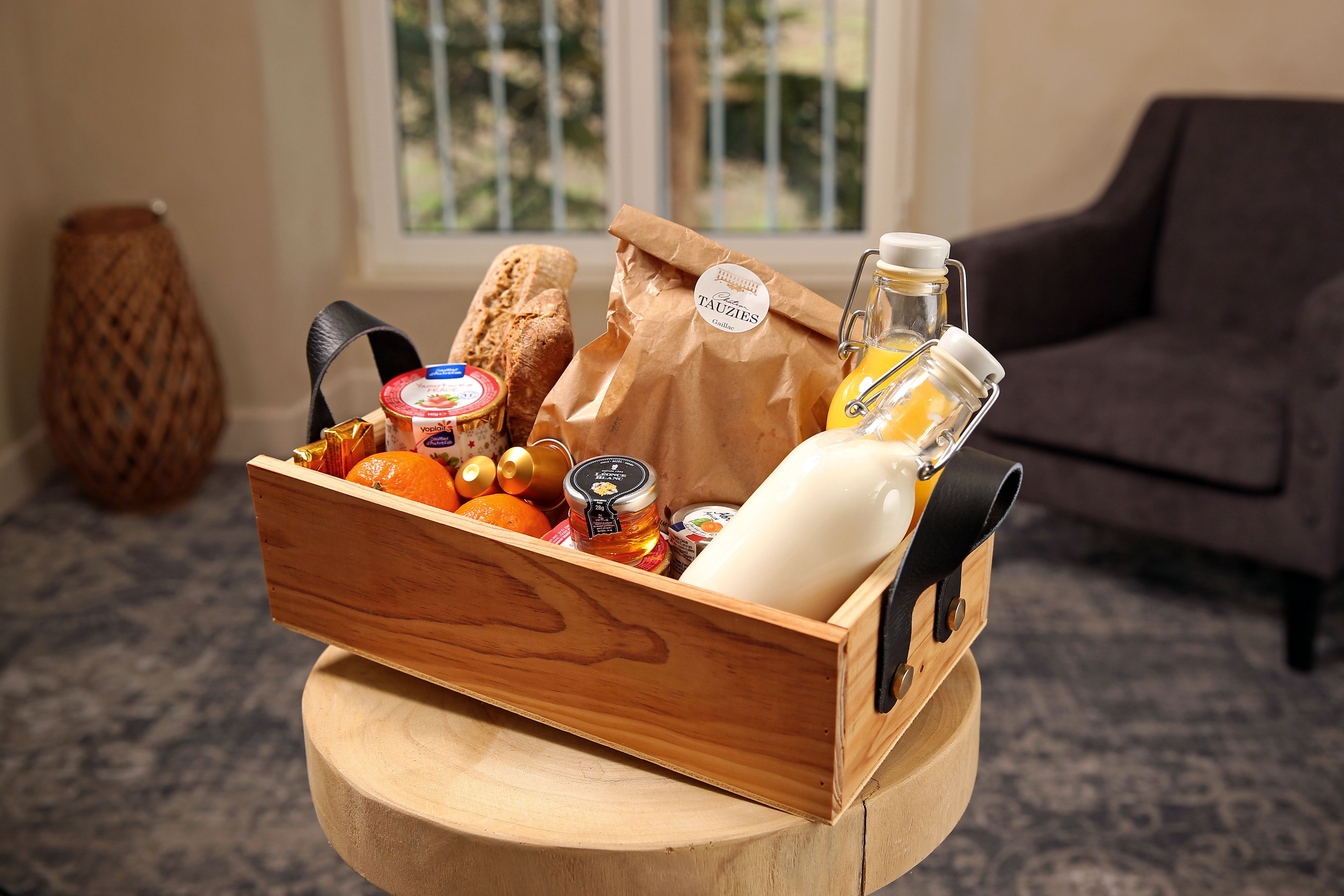 A wooden box with a variety of food items and a bottle of juice on a round wooden table.