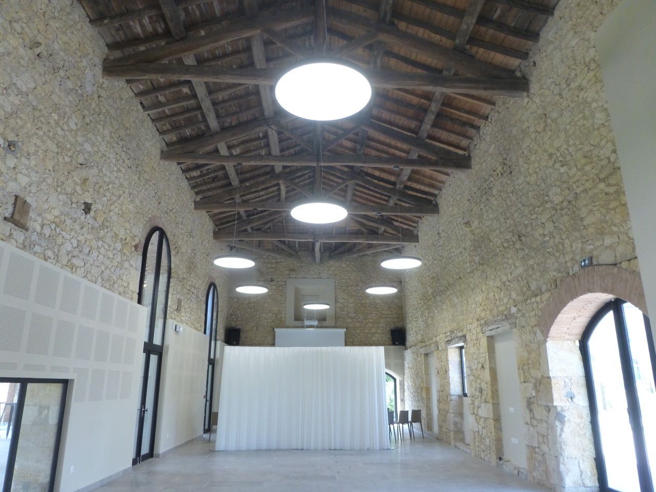 Un vaste hall doté d’un plafond haut, de murs en pierre et de plusieurs luminaires circulaires.