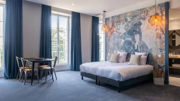 A modern bedroom with a large bed, a desk with chairs, and a view of greenery outside.