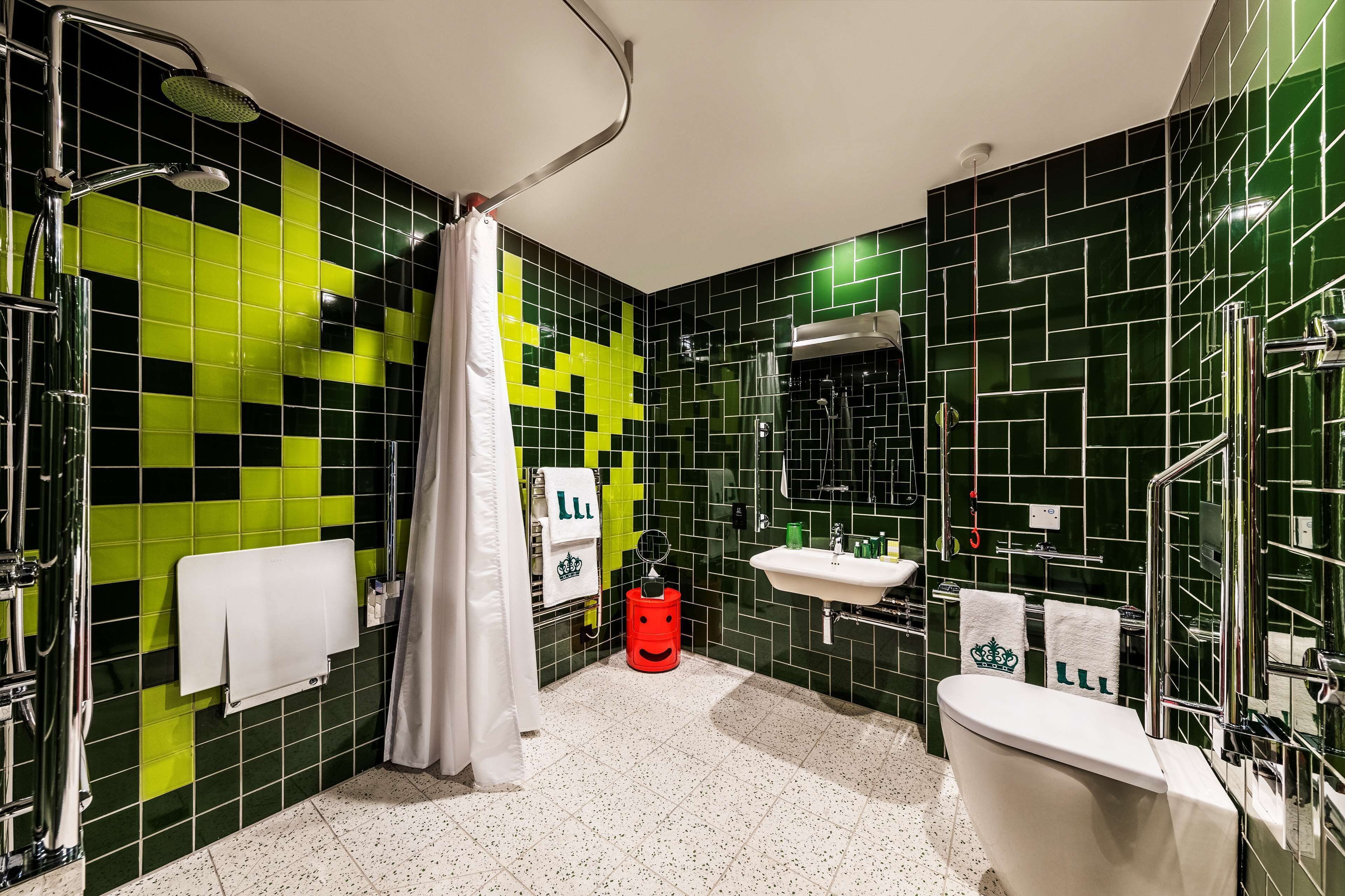 A bathroom with green and black tiled walls, a white sink, a white toilet, and a shower with a curtain.