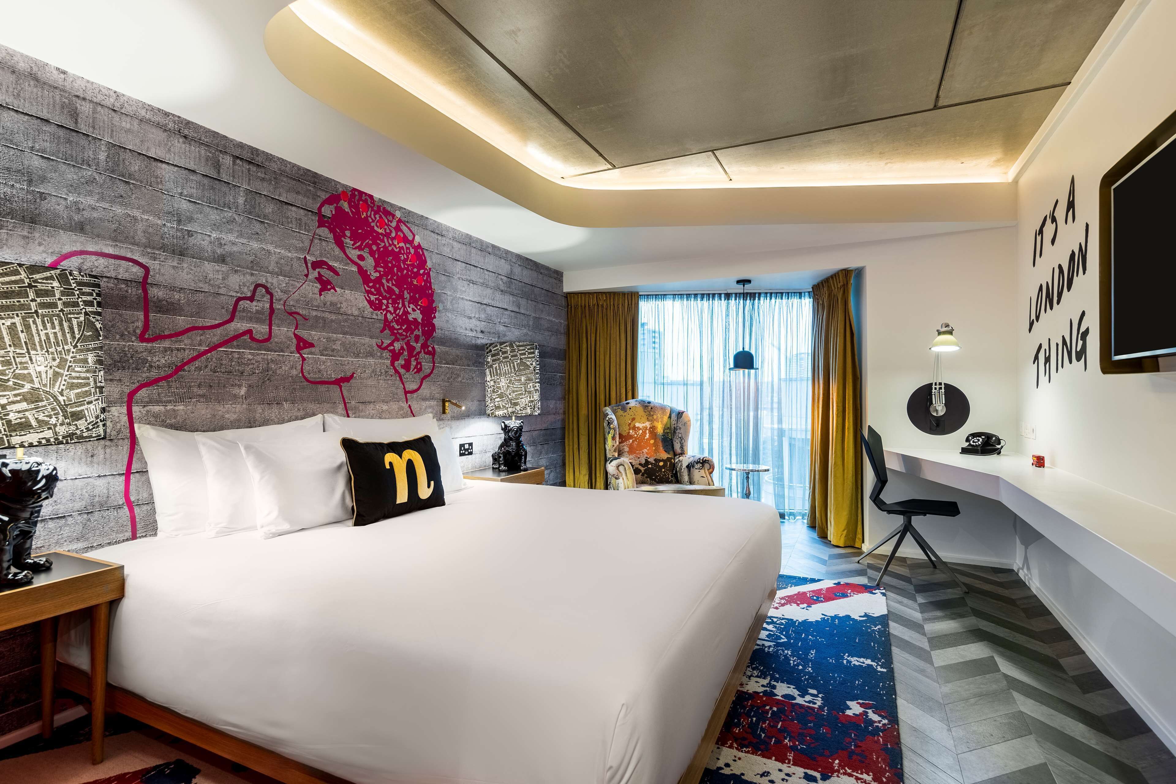 A modern hotel room with a large bed, a desk, a chair, and a view of the city.