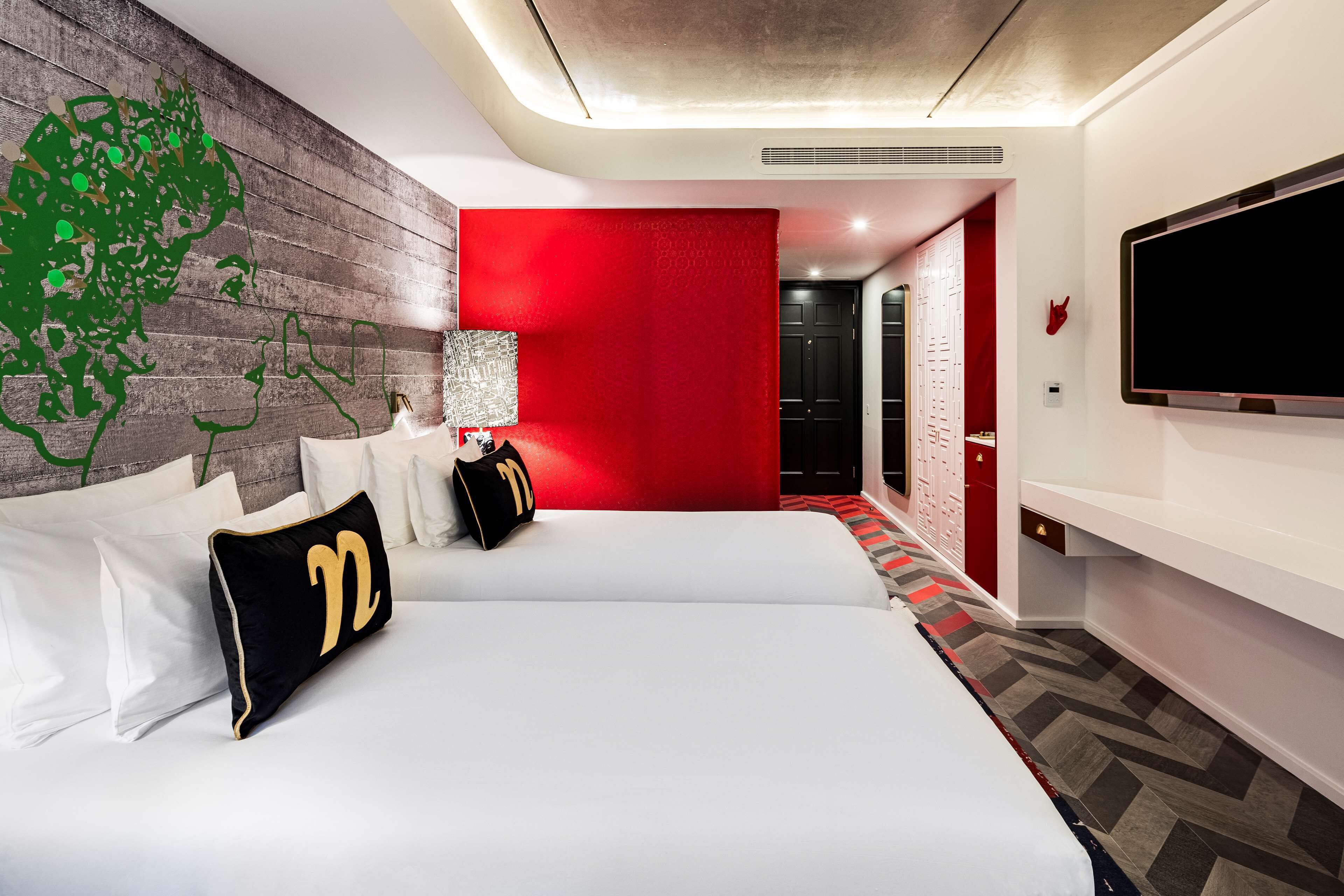 Una habitación de hotel con una cama grande, un televisor montado en la pared y una pared de acento roja.