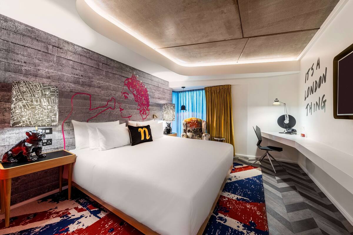 A modern hotel room with a large bed, a desk, and a chair. There is a map on the wall and a quote on the side.