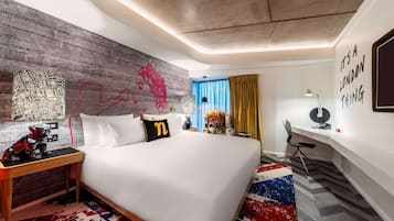 A modern hotel room with a large bed, a desk, and a chair. There is a map on the wall and a quote on the side.