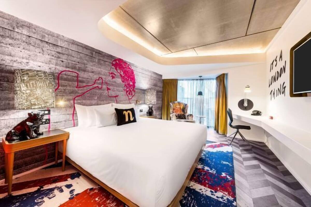 A modern hotel room with a large bed, a wooden headboard, a wall-mounted TV, and a view of the city.