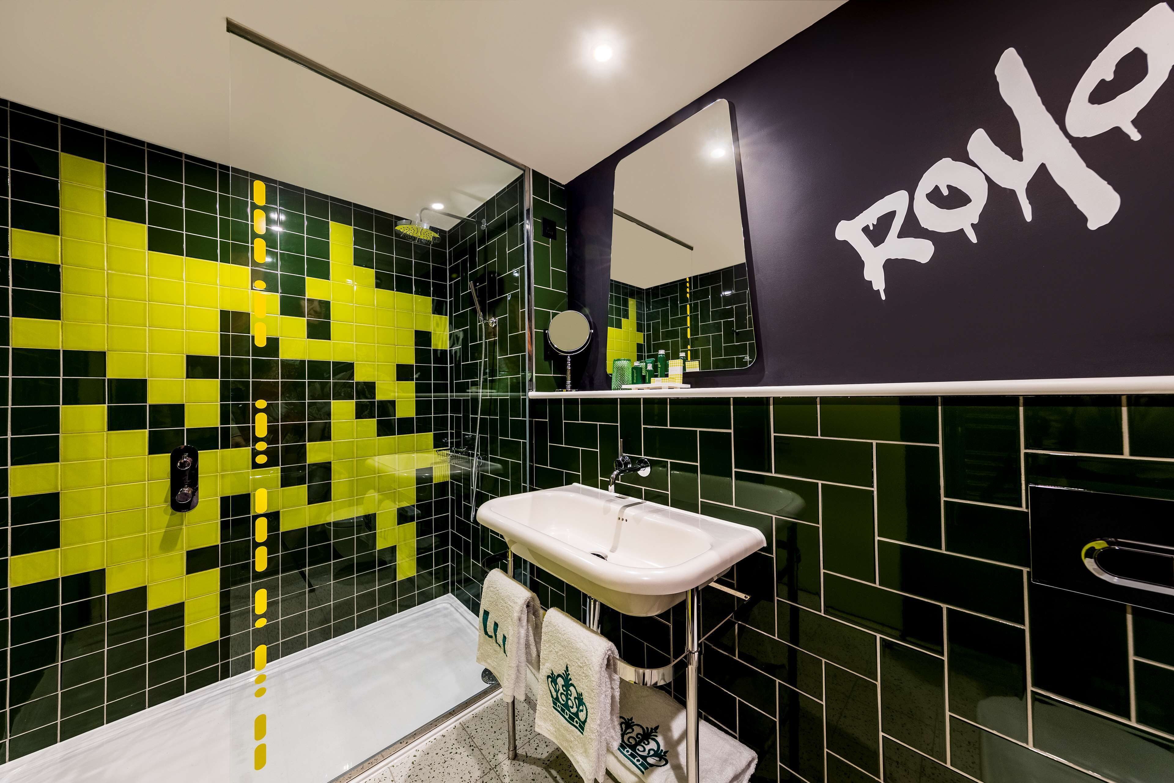 A modern bathroom with a black and yellow tiled wall, a white sink, and a mirror with the word "ROYAL" on it.