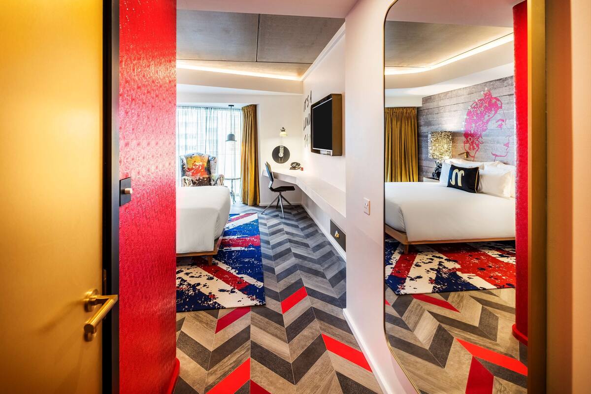 A hotel room with a bed, a desk, a chair, a TV, and a mirror.