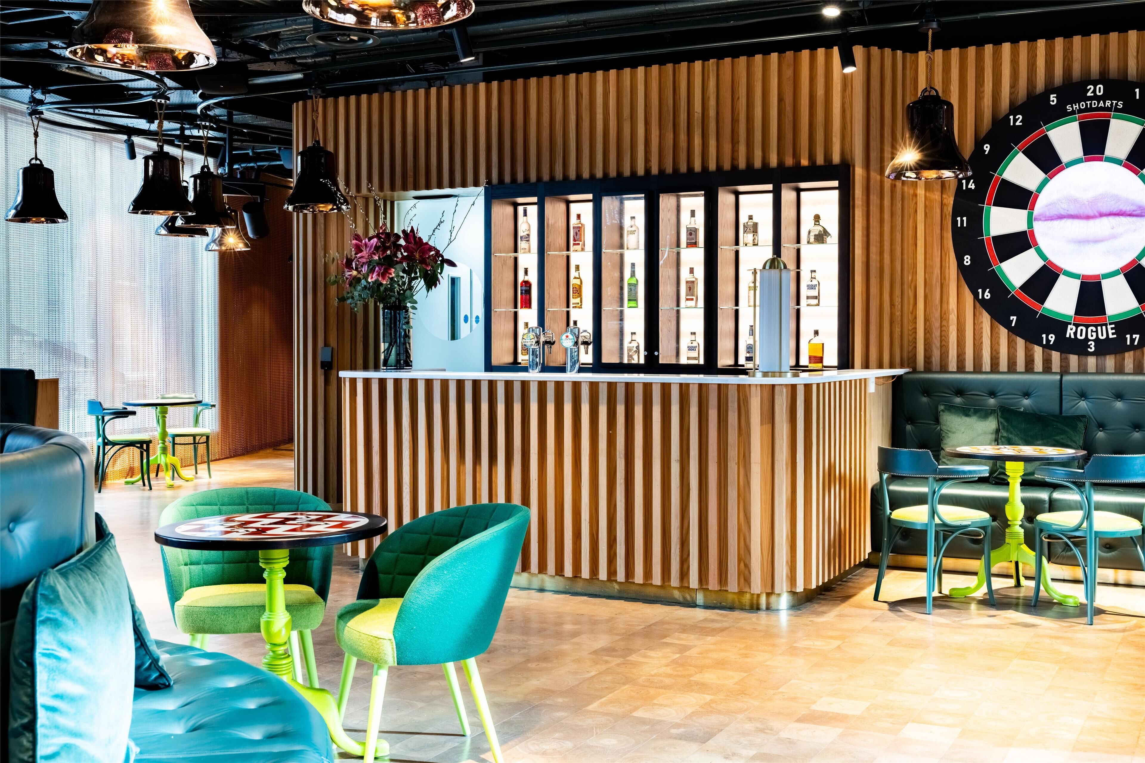 A bar area with a dartboard, bar counter, and seating with green chairs and a sofa.